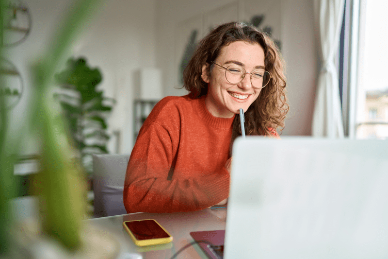 Happy young woman using laptop sitting at desk writing notes while watching webinar, studying online, looking at pc screen learning web classes or having virtual call meeting remote working from home.